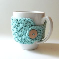 a crocheted coffee cup holder with a button on the front and bottom, sitting on a white surface