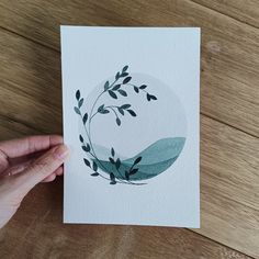 a hand is holding up a card with leaves on it and watercolors in the background