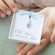 a person holding a small blue heart in a white box with a ribbon around it