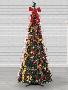 a decorated christmas tree in front of a white brick wall with red and gold ribbons