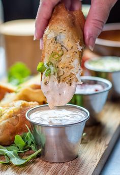 a person dipping something into a small metal cup on a cutting board with other food items