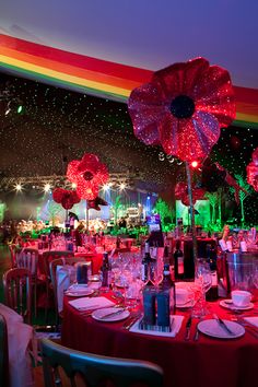 a room filled with lots of tables covered in red and white table cloths under a rainbow colored sky