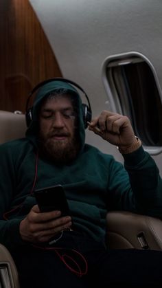 a man sitting in an airplane wearing headphones and listening to music on his cell phone