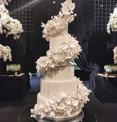 a large white wedding cake with flowers on the top and bottom tier is sitting on a black table