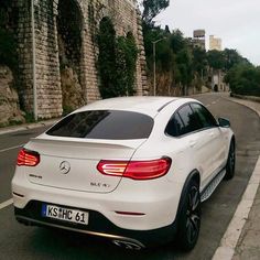 the rear end of a white mercedes c - class coupe driving down a road in front of an old brick wall