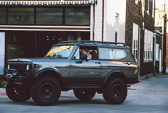 an suv parked in front of a building on the side of the road with people inside