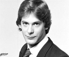 a black and white photo of a young man in a suit with his hair pulled back