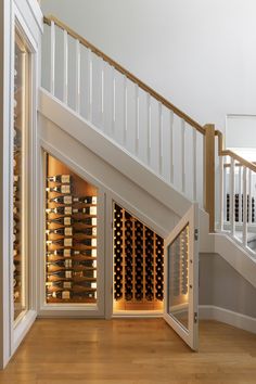 an open wine cellar under the stairs in a room with wooden floors and white railings