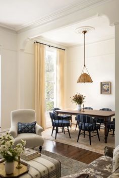 a living room filled with furniture and a dining table surrounded by windows covered in curtains