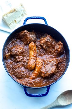 a blue pan filled with meat and sauce next to bread on a white counter top