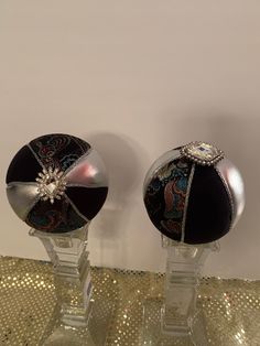 two glass vases with black and silver decorations on top of each one, sitting on a gold sequin table cloth