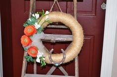 a wreath with orange flowers hanging on a wooden ladder in front of a red door