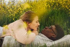 a man and woman laying on the ground in tall grass with yellow flowers behind them