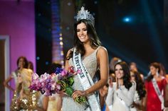 a beautiful young woman holding a bouquet of flowers in front of other women on stage