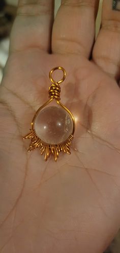 a hand holding a small gold pendant with a large stone in it's center