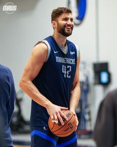 a man holding a basketball while standing on top of a gym floor in front of other people