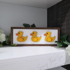 three yellow rubber ducks sitting on top of a white shelf next to flowers and greenery