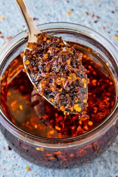 a spoon full of food sitting on top of a glass jar filled with liquid and spices