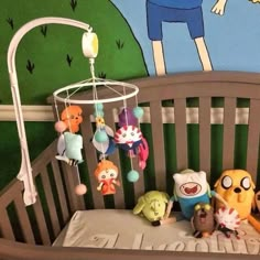 a baby crib with stuffed animals and toys hanging from it's sides in front of a cartoon themed wall