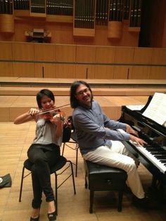 two people sitting at a piano and playing the violin