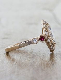 a diamond and ruby ring sitting on top of a wooden table