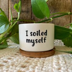 a coffee mug with the words i soiled my self on it sitting next to a plant