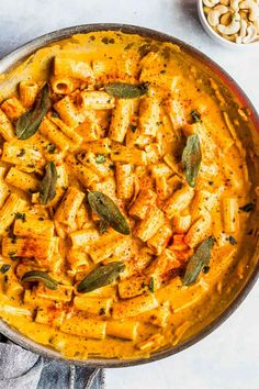 a pan filled with pasta and sage leaves on top of a white table next to bowls of macaroni and cheese