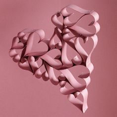 a heart shaped sculpture hanging from the side of a wall in front of a pink background