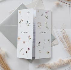 two folded cards with flowers on them sitting next to an envelope and some dried grass