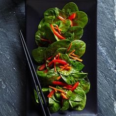 a black plate topped with lettuce and red peppers next to chopsticks