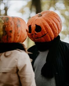 two people with pumpkins on their heads looking at each other in front of trees