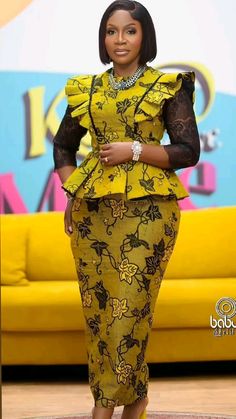 a woman in a yellow and black dress standing on a carpet with a couch behind her