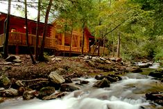 a cabin in the woods next to a river with rocks and water running through it