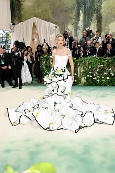 a woman in a white and green dress standing on a runway with cameras around her