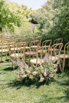 rows of wooden chairs sitting on top of a lush green field next to flowers and trees