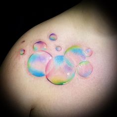 a woman's breast with colorful water drops on her left shoulder and right breast