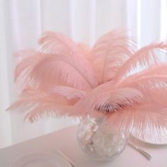 a vase filled with pink feathers sitting on top of a table next to a plate