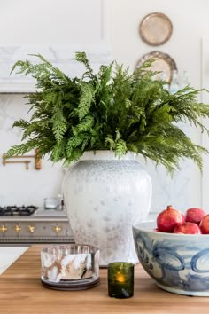 a white vase sitting on top of a wooden table next to a bowl of fruit