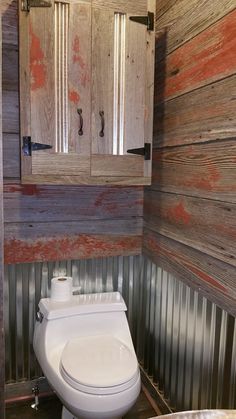 a white toilet sitting inside of a bathroom next to a wooden wall