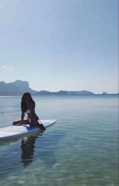 a woman is sitting on a surfboard in the water with mountains in the background