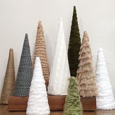 small knitted christmas trees are lined up in a row on a wooden shelf against a white wall