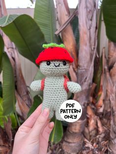 a hand holding a small crocheted stuffed animal with a red hat on it's head