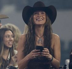 a woman wearing a cowboy hat and holding a cell phone in front of other women