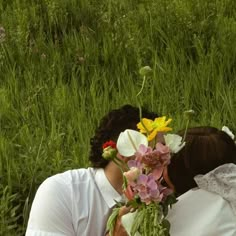 a couple kissing in the grass with flowers on their heads and one woman wearing a white dress