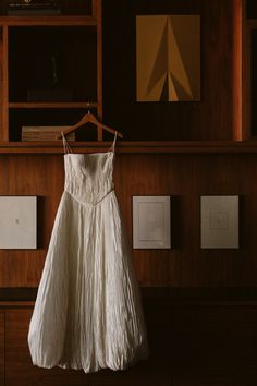 a white dress hanging on a wooden shelf in front of bookshelves and pictures