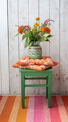 a green stool with flowers on top of it and a colorful striped rug in the background