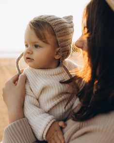 a woman holding a baby in her arms and wearing a knitted hat on top of her head