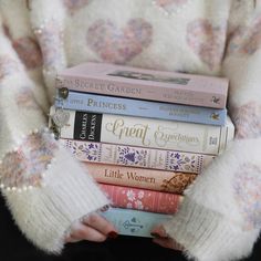 a woman is holding four books in her hands while wearing white sweaters and pink gloves