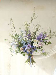 a woman holding a bouquet of blue and white flowers in her hands with the sun shining on her face