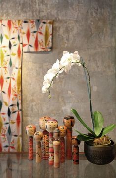 an orchid in a pot next to some wooden dolls